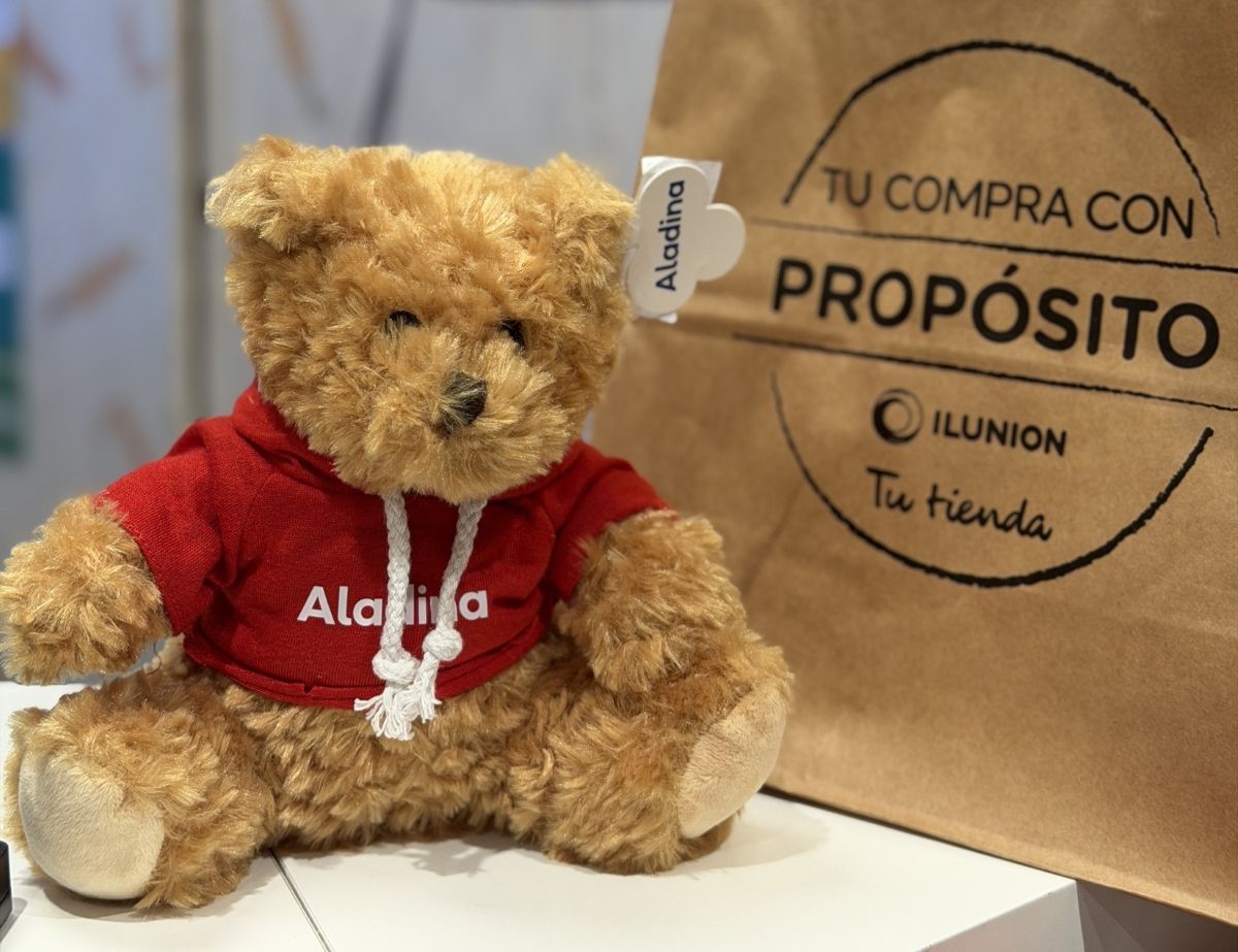 Un oso de peluche con el logotipo de la Fundación Aladina junto a una bolsa de Ilunion Tu Tienda