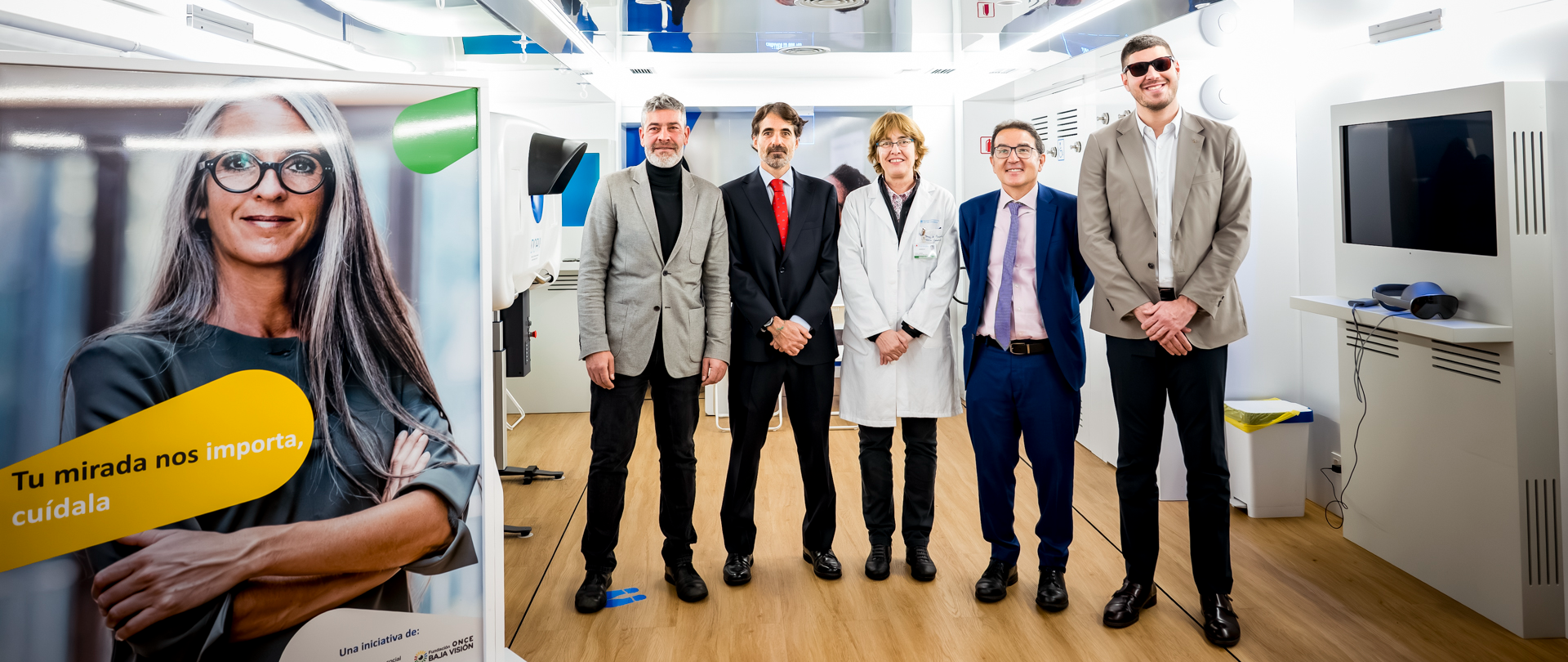 Foto de cinco personas al lado de un cartel dentro de la Unidad Móvil de salud visual